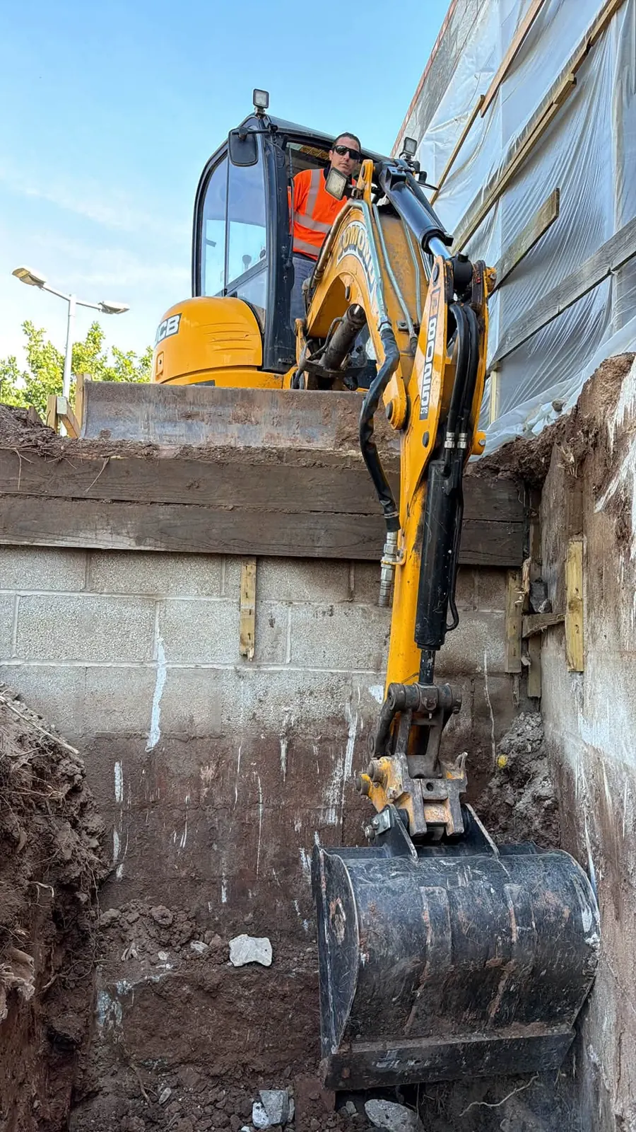 Tracked mini excavator digging a trench beside a wall, GRW Homes groundworks on a school project