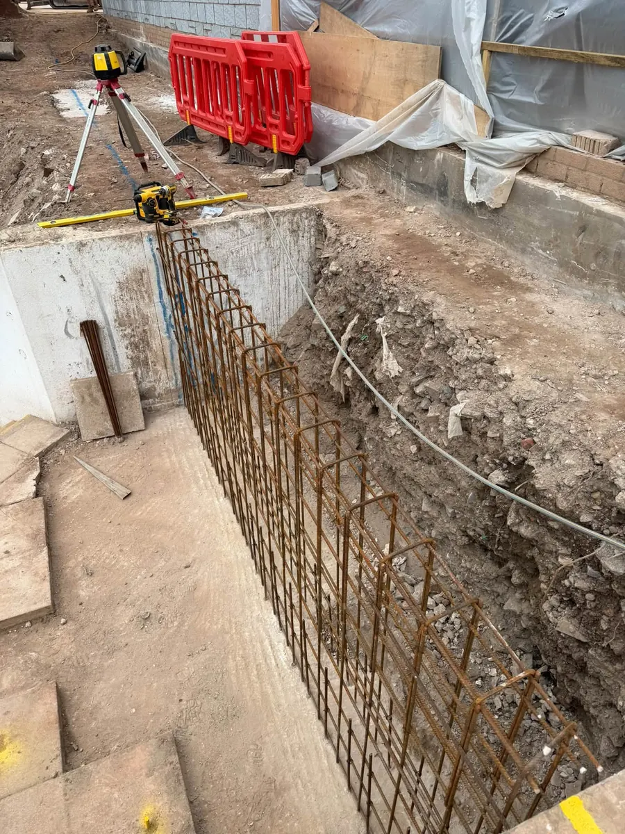 Retaining wall reinforcement set against an excavated bank with a laser level, GRW Homes groundworks on a school project